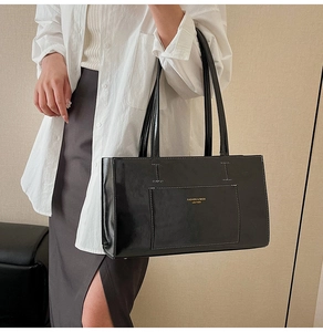 Detail of glossy black tote bag with white stitching and brand logo shown on model