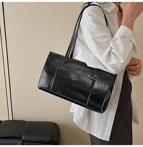 Detail of black glossy leather tote bag with white contrast stitching and gold logo