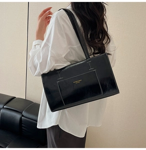 Detail of glossy black tote bag with white contrast stitching and gold lettering