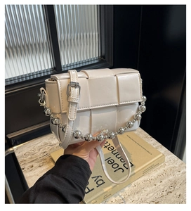 Detail of white woven grid crossbody bag featuring metallic silver ball chain and leather strap