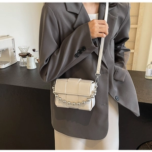 Detail of white woven crossbody bag with chain strap shown on a model in a cafe