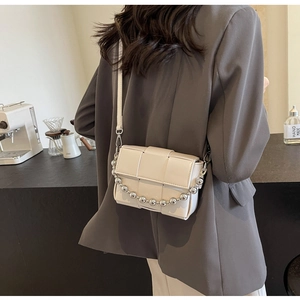 Model wearing a cream woven crossbody bag with stylish silver bead chain detail