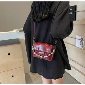Detail of woven burgundy crossbody bag with silver bead chain and glossy finish