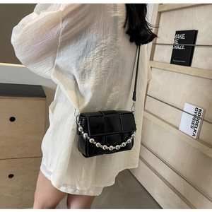 Detail of black woven crossbody bag with silver metal chain on minimalist background