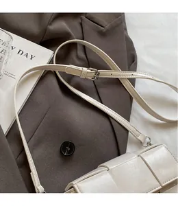 Close-up of cream woven shoulder bag with adjustable strap and metal buckle detail