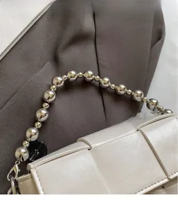 Detailed view of woven cream handbag featuring chunky silver beaded handle and leather texture