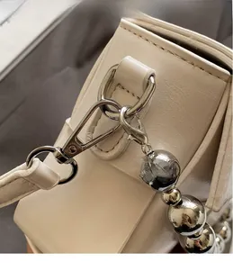 Detailed close-up of polished silver hardware hook and large beaded metal chain on bag