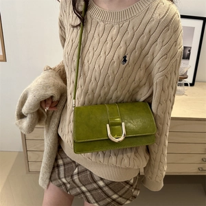 Sac sous le bras en cuir vert avec boucle dorée en U porté avec un pull en maille beige