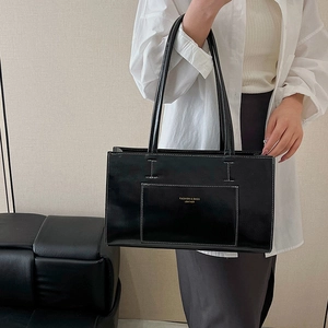 Minimalist black leather tote bag with white contrast stitching and long shoulder straps