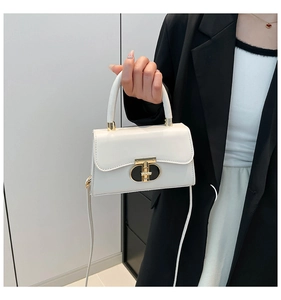 Close-up of cream crossbody bag featuring a golden semicircular rotating lock and fine stitching