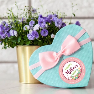 Detail of Happy Mother's Day floral sticker on a blue heart-shaped gift box with pink ribbon
