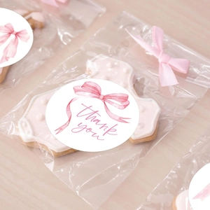 Detail of pink bow 'Thank You' stickers sealing clear cookie bags on a wooden surface