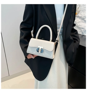 Detail of minimalist cream handbag with oval metal clasp on black blazer outfit