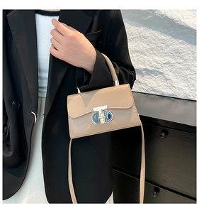 Detail of elegant beige crossbody bag with large golden T-shaped metal clasp and strap