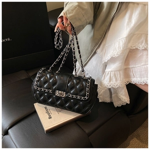 Detailed view of black quilted flap bag with silver chain strap held by a model