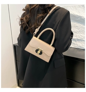 Detail view of beige crossbody bag with gold buckle and top handle worn with a black suit