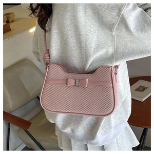 Détail du sac baguette rose tissé avec nœud et bandoulière réglable porté à l'épaule