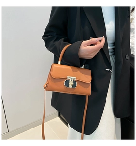 Close-up of caramel leather handbag featuring a gold metal buckle and hand-held handle