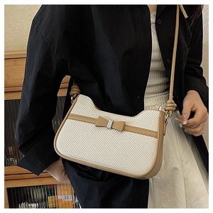 Détail du sac tissé crème avec bordure marron et nœud en cuir sur le modèle