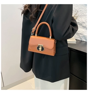 Brown leather crossbody bag detail with metal buckle and shoulder strap worn by model