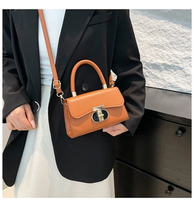 Detail of a brown square crossbody bag with a gold T-lock shown on a fashion model