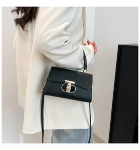 Detail of black top handle bag with gold hardware worn over a stylish white blazer