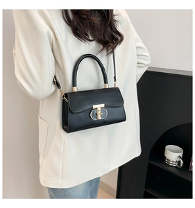 Detail of a black leather handbag with gold clasp worn over a white blazer
