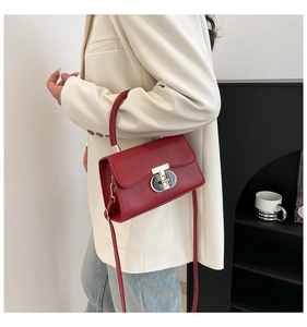 Red leather handbag with gold T-lock shown on a model wearing white blazer and jeans