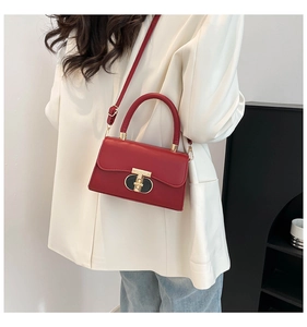 Detail shot of a red leather crossbody bag featuring a gold T-bar metal lock and shoulder strap