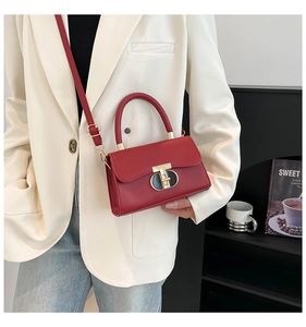 Detail of red square handbag with gold metal lock worn by model in white suit