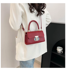 Detail of burgundy leather handbag featuring a vintage gold T-lock and white blazer contrast