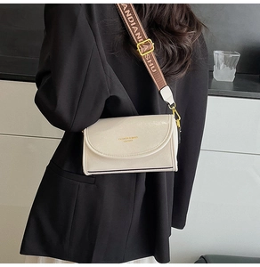 Detail of cream crossbody bag with wide brown patterned strap on a black blazer
