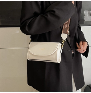 Detail of a beige crossbody bag with wide jacquard strap worn over a black blazer