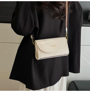 Detail of cream leather crossbody bag with branded wide strap on a black blazer