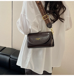 Detail of dark brown leather crossbody bag with wide logo strap worn by a model