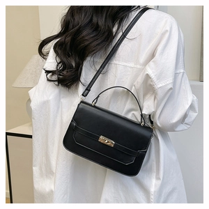 Detail view of black leather handbag with gold twist lock worn as a crossbody bag