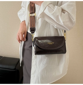 Detail of dark brown leather crossbody bag featuring a jacquard strap and gold buckle