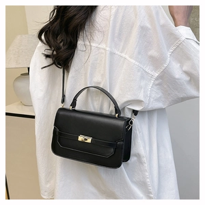 Detailed view of black minimalist crossbody bag with golden twist lock and textured finish