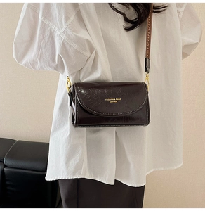 Detail of dark brown crinkled leather bag with wide strap and golden hardware
