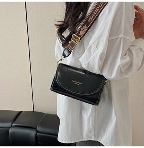 Detail of black crossbody bag with wide ethnic shoulder strap and gold logo engraving