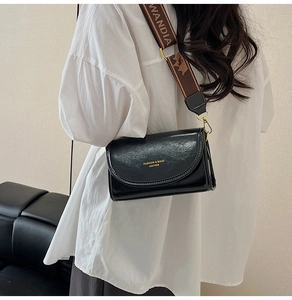 Detail of black faux leather crossbody bag with wide brown patterned strap and gold hardware