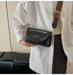 Close-up of black crossbody bag with wide printed strap and golden metal buckle