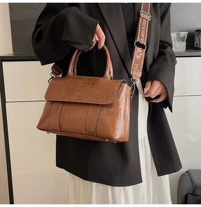 Close-up of brown crocodile pattern flap and wide textile strap on a leather tote bag