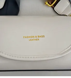 Detail of cream white leather bag showing the golden branded logo and pebbled texture