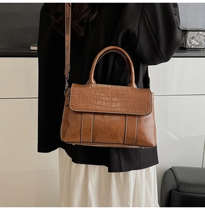Detail of crocodile-embossed brown leather handbag with a patterned wide strap