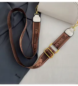 Close-up of a white crescent crossbody bag with a wide jacquard strap and gold hardware
