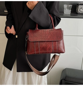 Detail of burgundy crocodile-embossed tote bag with branded wide fabric shoulder strap