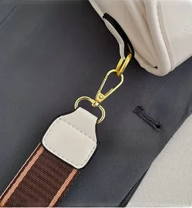 Detail of white leather bag featuring gold hardware hook and striped fabric strap