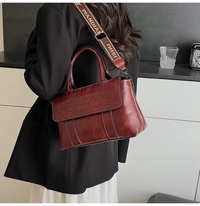 Detail of burgundy crocodile-embossed leather handbag with wide logo strap and stitching