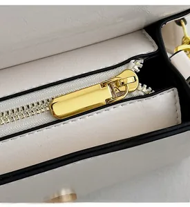 Close-up of golden metal zipper and neat stitching on white leather crossbody bag